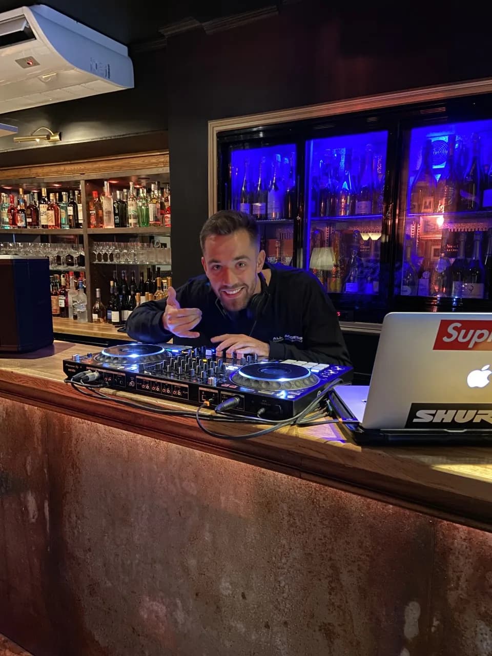 DJAY LEMON en chemise blanche derrière ses platines, ambiance salle blanche.