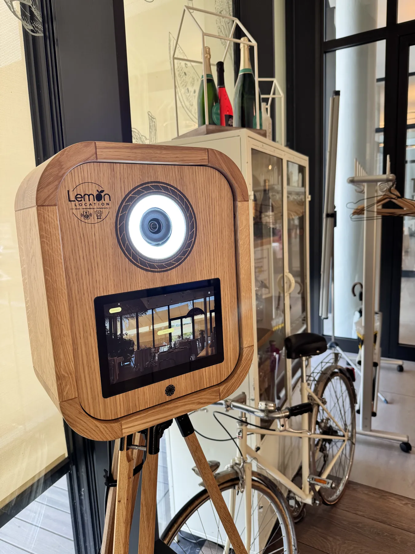 La borne photo LEMON LOCATION en chêne massif : anneau lumineux, écran tactile et logo gravé, installée sur son trépied en bois.